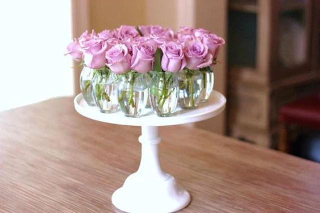 a cake stand with small glass vases and single roses in each one