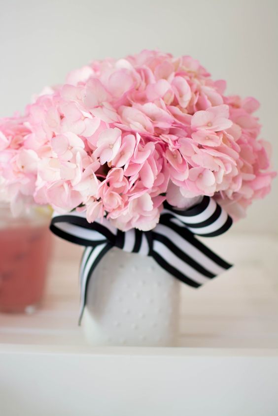 a neutral vase with a striped black and white bow and pink flowers