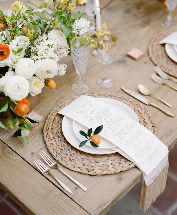 this tablescape is accentuated with creamy and orange flowers, fruit and a wicker placemat