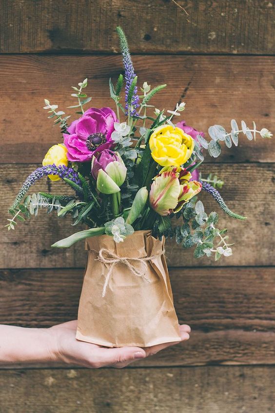 a colorful bouquet with eucalyptus in a vase with a paper sack