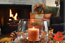a basket with faux pumpkins and berries and a glass with a candle and pebbles for the fall