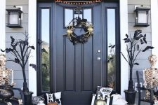 a chic classic Halloween porch with black trees with bats, a spider wreath, white, orange and gold pumpkins and lanterns