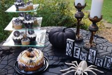 a classic Halloween dessert table with a whimsy black tablecloth, spiders, a black pumpkin and pillar candles
