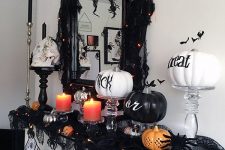 a classic Halloween mantel with lights, black and orange candles, black and white pumpkins, a printed bunting and spiders