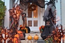 a classic Halloween porch with a ghost, lights on mini trees, potted blooms, black fabric and giant spiders plus pumpkins