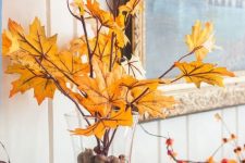 a glass filled with acorns and with branches with yellow leaves and blooming branches make the mantel look very bold and fall-like