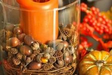 a glass with vine, acorns and nuts and an orange pillar candle is a cool and easy rustic decoration