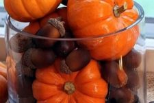 a large glass with acorns and pumpkins is a cool and very easy fall decoration that you can make last minute