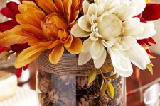 a large glass with pinecones and twine, with bright, red and white blooms is a cool fall arrangement