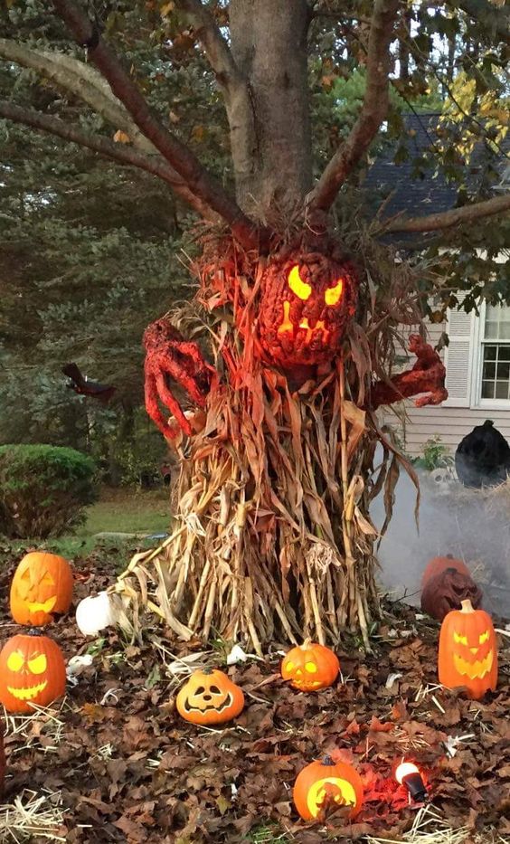 a scary outdoor decoration of corn husks, pumpkin lanterns, a bloody pumpkin and hands is fantastic