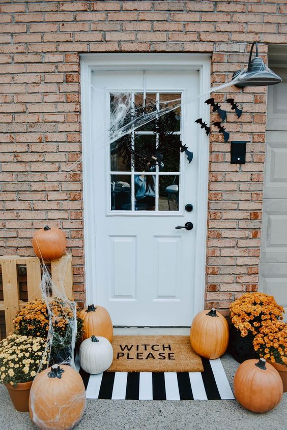 a stylish Halloween front porch with orange pumpkins, bats, web and bright potted flowers