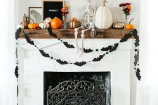 a stylish rustic Halloween mantel with black balloons, a bat bunting, lots of pumpkins, a skeleton and blooms