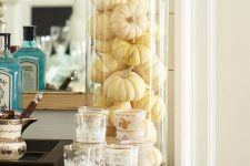 a tall and large glass vase filled with white pumpkins is a lovely and simple fall decoration for a chic natural touch