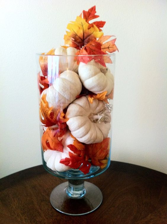 a tall glass with small pumpkins and bright leaves is an easy and cool fall decoration or centerpiece