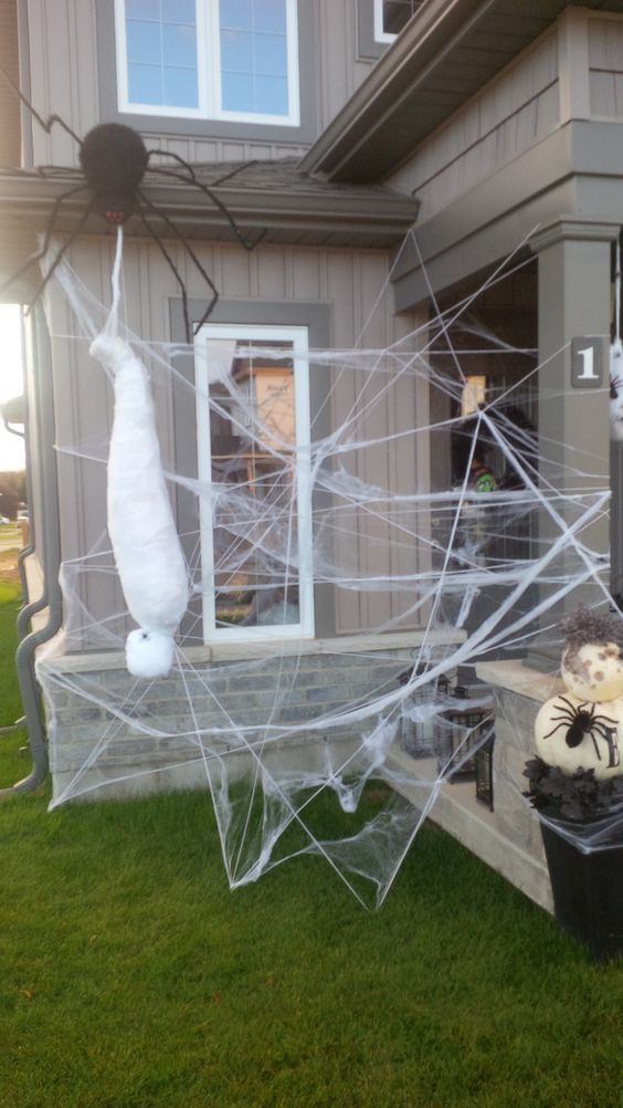 spooky outdoor Halloween decor with spiderwebs, spiders, a mummy and pumpkins all around