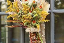 a dried fall arrangement with various blooms, corn husks and corn cobs and a burlap bow