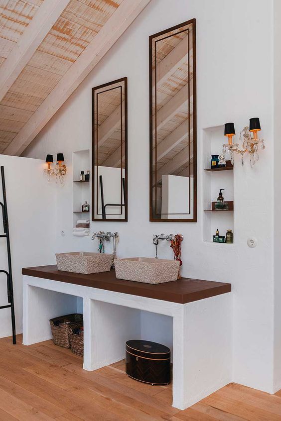 a bathroom with a vanity, stone sinks, niches with glass shelves, elegant sconces and tall mirrors