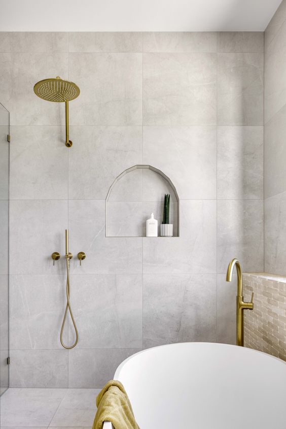 a contemporary bathroom clad with large scale tiles, an oval tub, an arched niche for decor and lovely brass fixtures