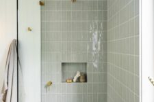 a grey shower space clad with skinny tiles, with a sleek niche for decor and brass fixtures is a lovely space