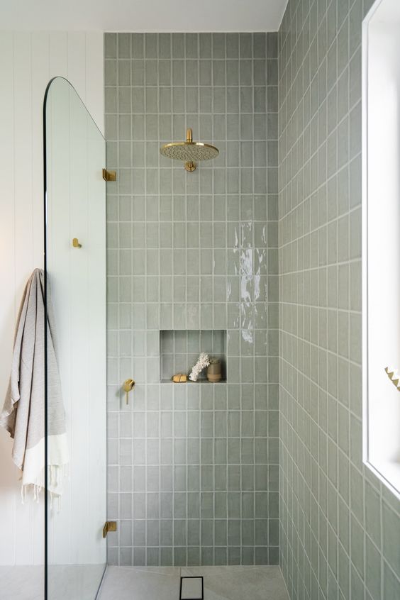 a grey shower space clad with skinny tiles, with a sleek niche for decor and brass fixtures is a lovely space