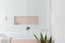 a lovely bathroom with white and pink skinny tiles, a niche over the tub that is used for decor and a potted plant