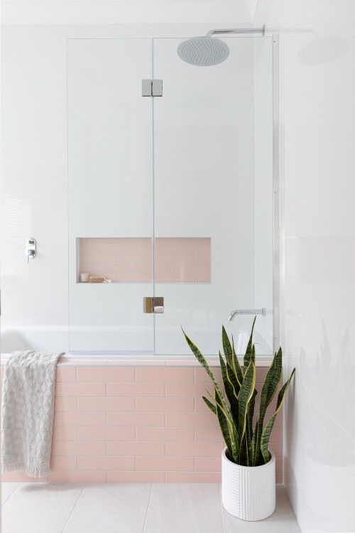 a lovely bathroom with white and pink skinny tiles, a niche over the tub that is used for decor and a potted plant