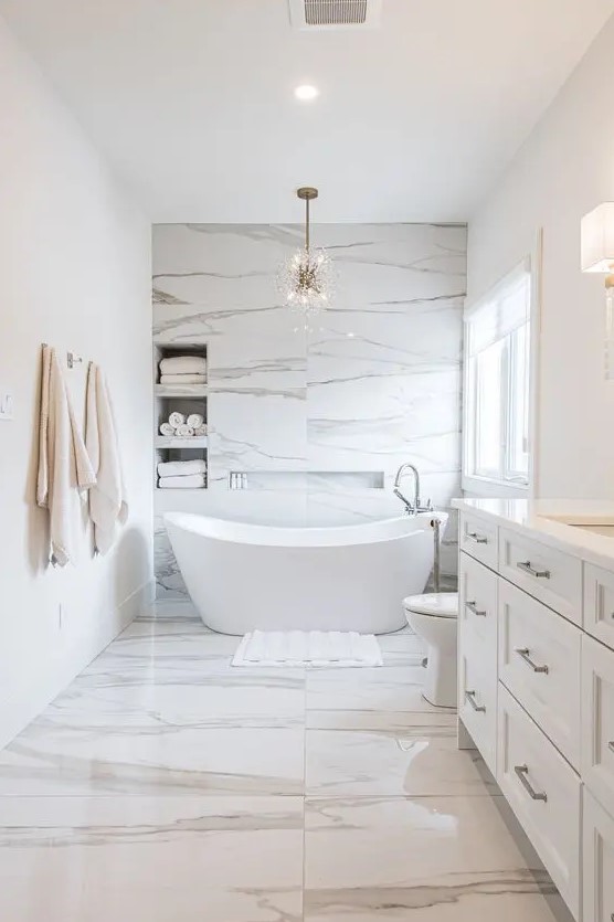 a minimalist luxurious bathroom clad with white marble, with niche shelves over the bathtub, an oval tub and a large vanity