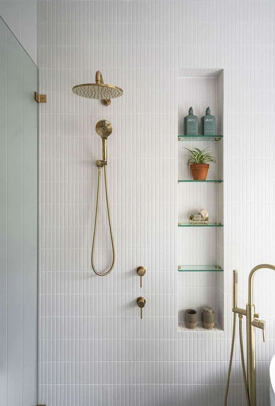 a minimalist neutral bathroom with a niche with glass shelves that are used mostly for decor and some brass fixtures