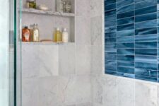 a modern bathroom clad with grey and blue marble tiles, a niche with shelves used for storing things, a built-in bench