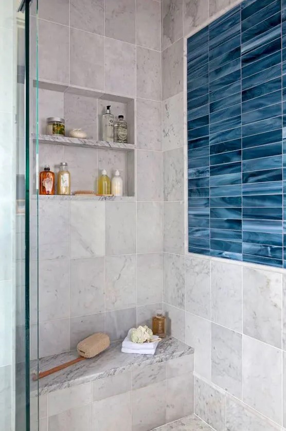 a modern bathroom clad with grey and blue marble tiles, a niche with shelves used for storing things, a built-in bench