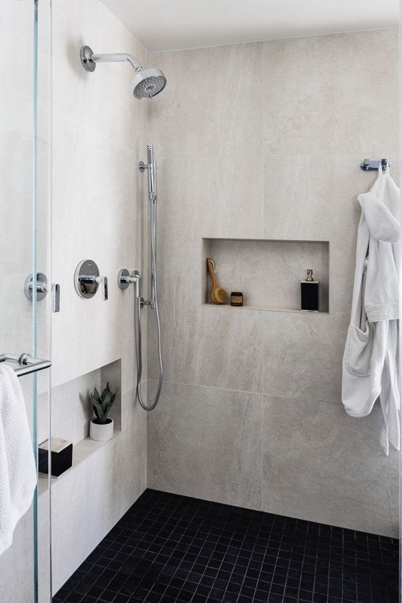 a modern bathroom clad with large scale stone and small scale black tiles, niches for decor and storage