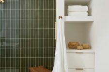 a modern bathroom done in neutrals and dark green skinny tiles, a deep niche with shelves and a built-in cabinet for storage