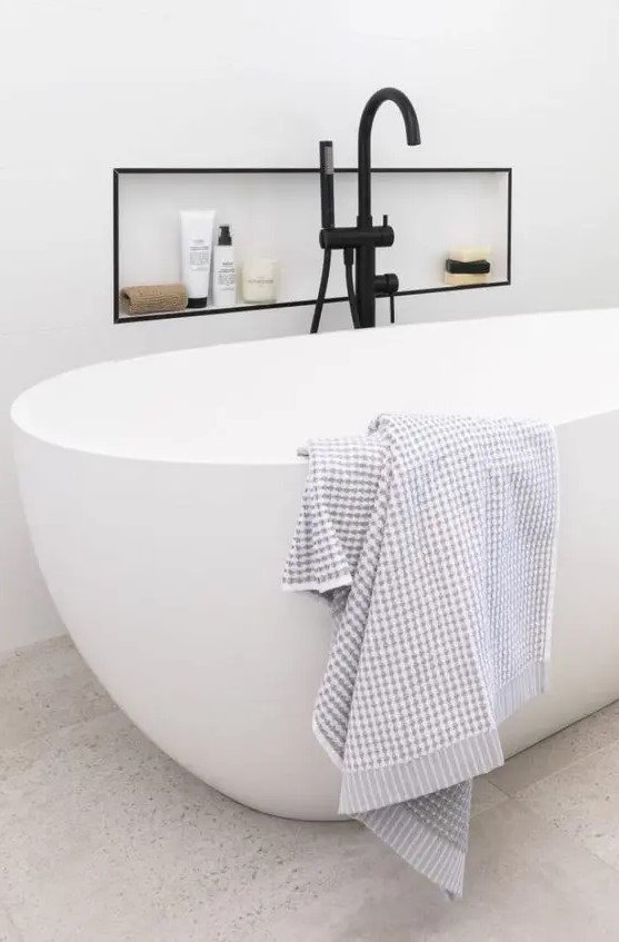 a modern bathroom with a an oval tub, a niche with a black frame to accent it, to store some stuff and a black faucet