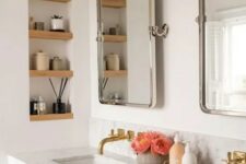 a modern bathroom with a double vanity and sinks, mirrors, a niche with wooden shelves and decor plus some blooms
