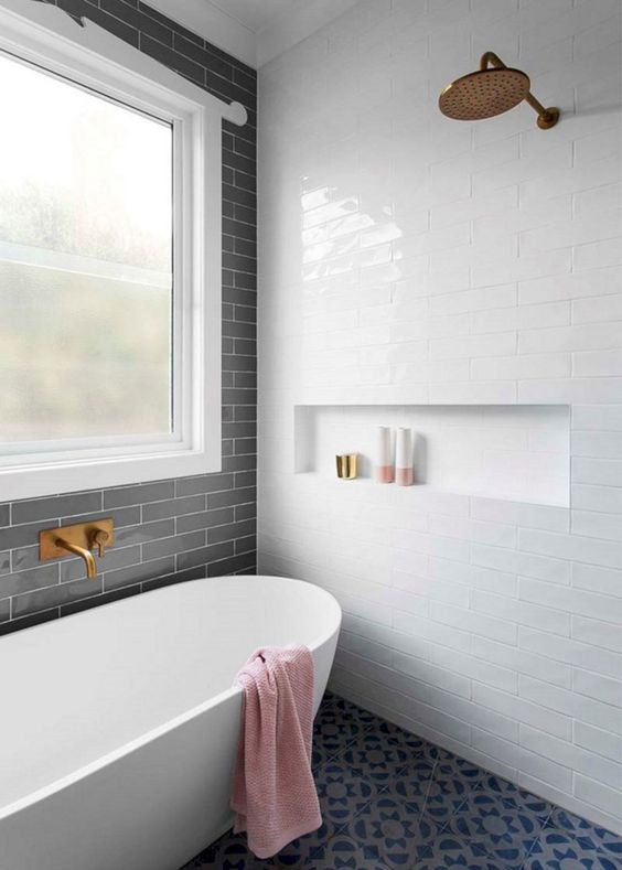 a modern bathroom with three types of tiles, an oval bathtub, a niche with bathroom stuff and a window
