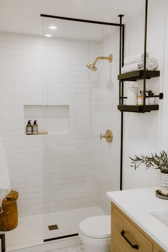 a modern farmhouse bathroom clad with skinny tiles, a timber vanity, black shelves and black handles, a niche in the shower