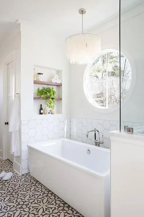 a modern neutral bathroom with white walls, printed and hexagon tiles, a rectangular tub, a niche with shelves and some lovely decor