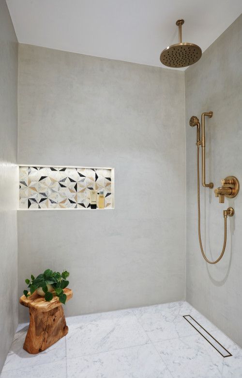 a modern shower space with a lit up colorful tile niche, brass fixtures, a wooden stool and a potted plant
