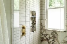 a modern shower space with marble and white skinny tiles, a niche for storage and gold fixtures is chic and refined