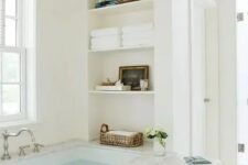 a neutral airy bathroom with a bathtub and niche shelves by its side is a cool idea, there you can store anything you want