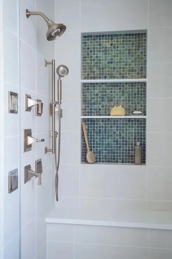 a neutral bathroom clad with tiles, with a niche shelf clad with green tiles, storing stuff for washing