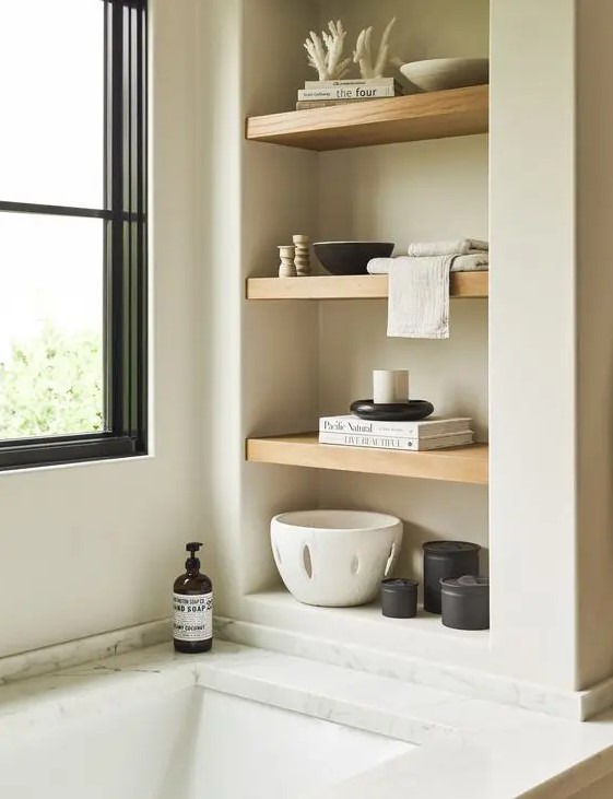 a neutral bathroom with a niche with wooden shelves used for placing decor there to make the bathroom look cooler