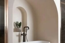 a neutral bathroom with an oval tub placed in a niche, with an additional niche with a potted plant looks jaw-dropping