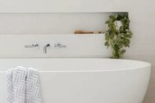 a neutral minimal bathroom clad with white subway tiles, with an oval tub, a niche shelf that is used mostly for decor
