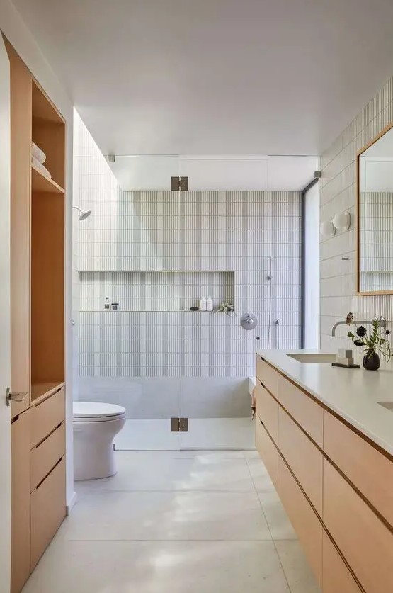 a neutral modern bathroom done with skinny and large scale tiles, a timber vanity and a storage unit, a niche for storage in the shower