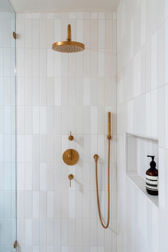 a neutral shower space clad with skinny tiles, with a niche for storage and brass fixtures is a cool and chic solution