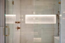 a neutral shower space clad with small and large scale tiles, with a lit up niche for storage and elegant brass fixtures