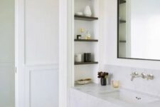 a refined bathroom with paneled walls, a printed floor, a built-in vanity of stone, a niche with shelves and lovely decor