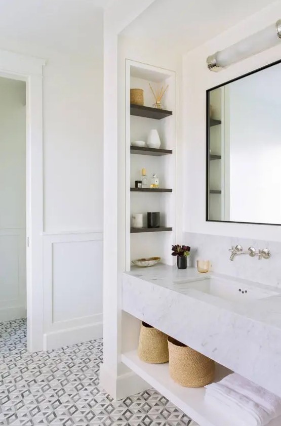 A refined bathroom with paneled walls, a printed floor, a built in vanity of stone, a niche with shelves and lovely decor