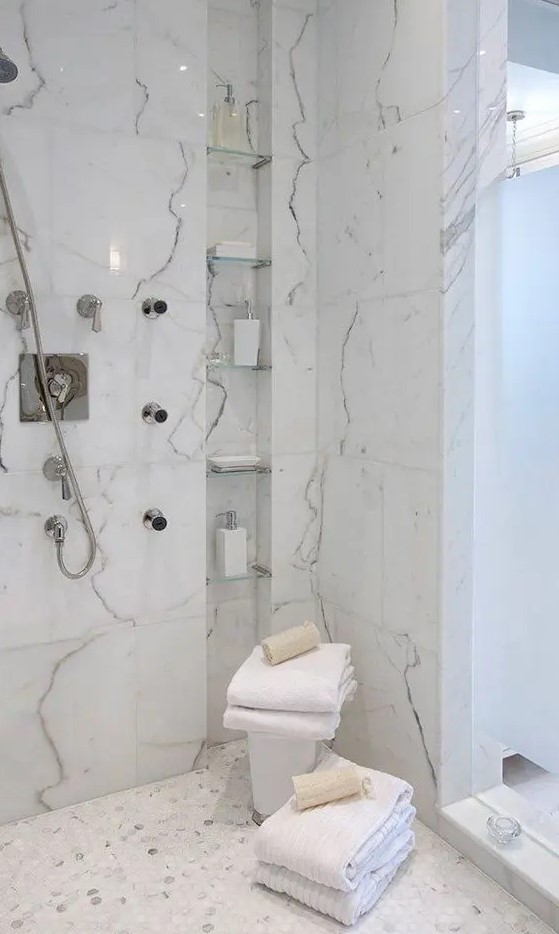 a refined shower with marble tiles, with a tall and narrow niche with shelves used for storing various stuff